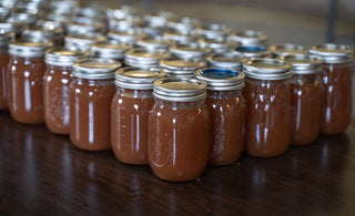 Numerous sealed Mason jars filled with homemade apple butter arranged in neat rows on a wooden table