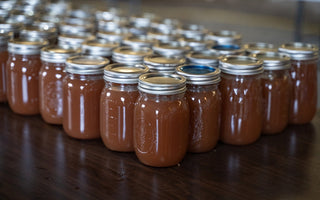 Numerous sealed Mason jars filled with homemade apple butter arranged in neat rows on a wooden table