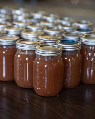 Numerous sealed Mason jars filled with homemade apple butter arranged in neat rows on a wooden table