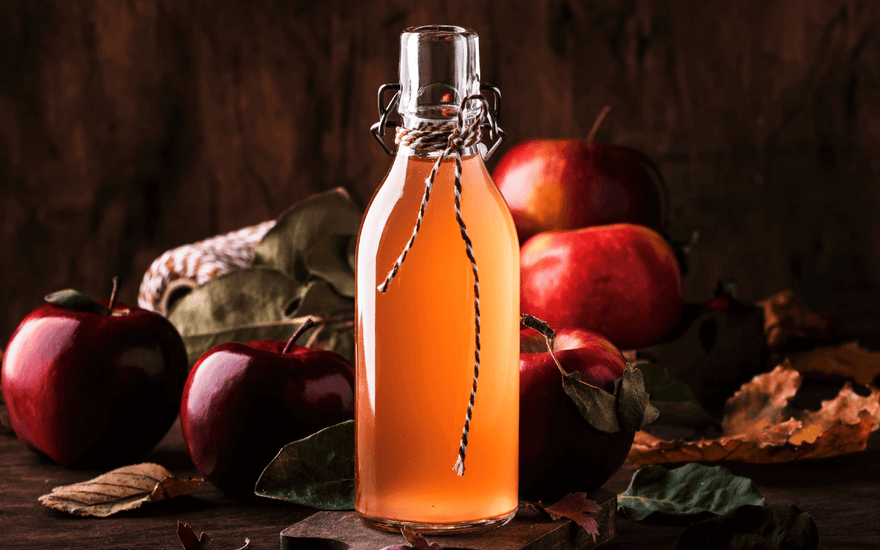 Image promoting "6 Amazing Recipes" for Bourbon Apple Cider, featuring a garnished glass of the drink on a wooden table.