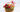 Fruit basket gift arrangement featuring fresh apples, oranges, kiwis, red carnations, and berries in a wicker basket with decorative red and white ribbon.